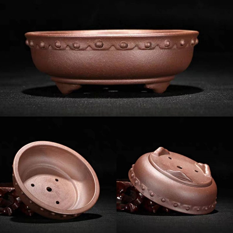 May include: A terracotta bonsai pot with a rounded shape and three legs. The pot has a decorative rim with small dots and a textured surface.