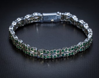 May include: A silver bracelet with a double row of emerald green gemstones. The bracelet has a clasp closure.