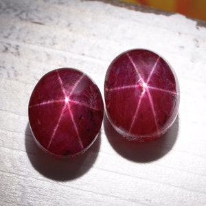 May include: Two round, red star ruby gemstones with a six-pointed star in the center.