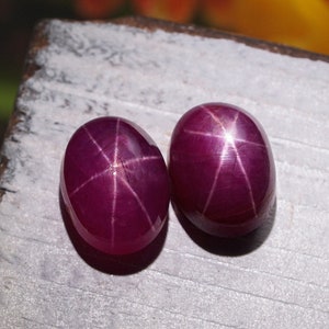 May include: Two oval-shaped, deep red star ruby gemstones with a six-pointed star pattern visible in the center of each stone.