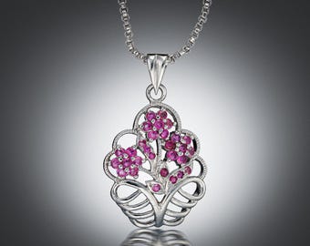 May include: Silver pendant necklace with a floral design and pink gemstones. The pendant showcases an openwork design with a stylized flower bouquet. The chain is a delicate, silver-toned cable chain.
