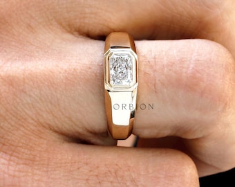 May include: A gold ring with a rectangular, clear gemstone. The ring has a thick band and a bezel setting. The gemstone is set in a white metal. The ring is on a hand against a black background. The word "ORBION" is visible on the ring.