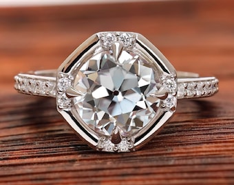 May include: A silver engagement ring with a large, round, clear diamond set in a hexagonal halo. The ring is surrounded by smaller diamonds and is set on a wooden surface. The word "ORBION" is printed below the ring.