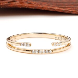 May include: A gold ring with a double band and a row of small diamonds. The ring is open on one side, creating a unique and modern design.