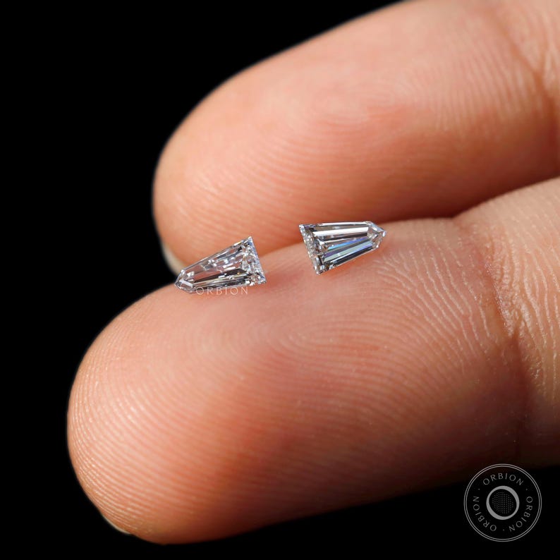 Puede incluir: Dos diamantes transparentes, facetados, de forma triangular en un dedo.