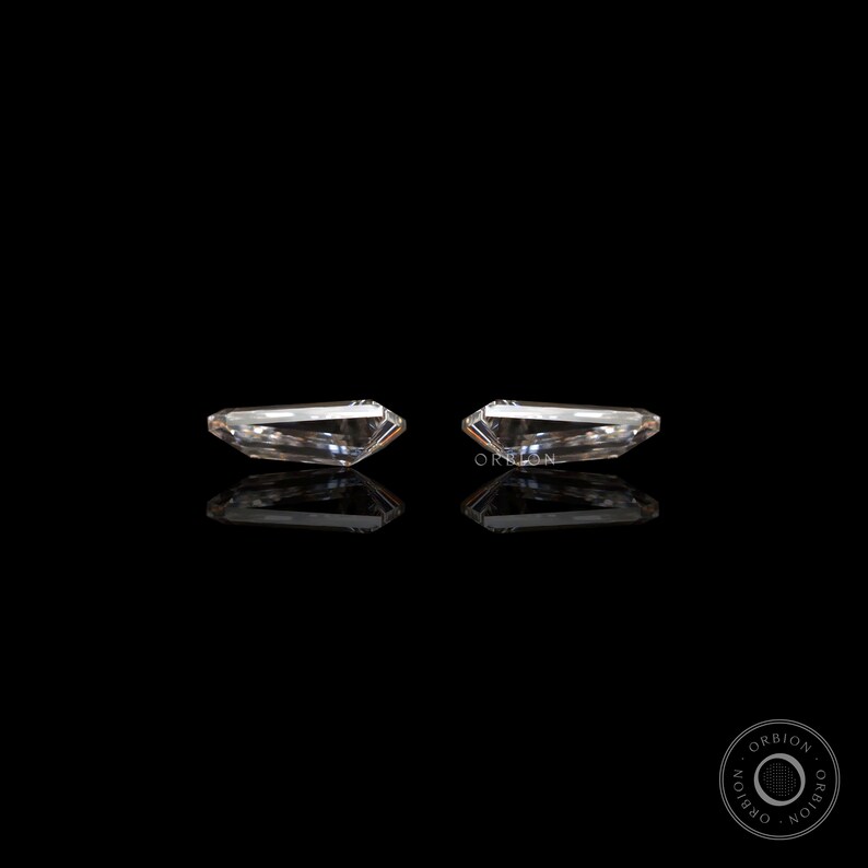 Puede incluir: Dos piedras preciosas rectangulares, transparentes y facetadas, engastadas en un marco plateado, se muestran sobre un fondo negro. Las piedras preciosas est&aacute;n colocadas una al lado de la otra, con sus lados largos paralelos entre s&iacute;.
