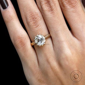 May include: A gold ring with a large, round, clear gemstone. The ring is on a person's finger.