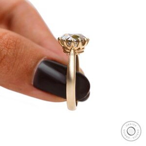 May include: A gold engagement ring with a round, clear gemstone set in a prong setting. The ring is on a finger and the band is smooth.