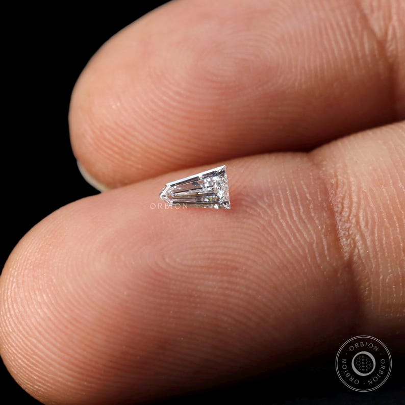 Puede incluir: Un diamante transparente, facetado, de forma triangular con una punta puntiaguda. El diamante est&aacute; colocado en un dedo para comparar el tama&ntilde;o.