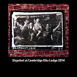 May include: Black and white photo of a band called Slapshot performing at the Cambridge Elks Lodge in 2014. The photo is framed and mounted on a brick wall.