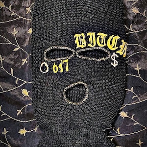 May include: Black ski mask with a gold embroidered design that says "BITCH" and "617" with a dollar sign.