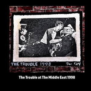 May include: Black and white photo of a band performing live on stage. The photo is framed and has the text "THE TROUBLE 1998" written on the bottom. The photo is set against a brick wall.