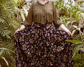 May include: A woman with red hair wearing a green blouse and a black and green floral skirt with a green trim.