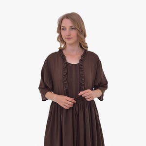 Pode incluir: Um vestido castanho com um casaco a condizer. O vestido tem um decote redondo com acabamento em folhos e um la&ccedil;o na cintura. O casaco tem mangas curtas e acabamento em folhos na frente.