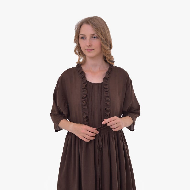 Pode incluir: Um vestido castanho com um casaco a condizer. O vestido tem um decote redondo com acabamento em folhos e um la&ccedil;o na cintura. O casaco tem mangas curtas e acabamento em folhos na frente.