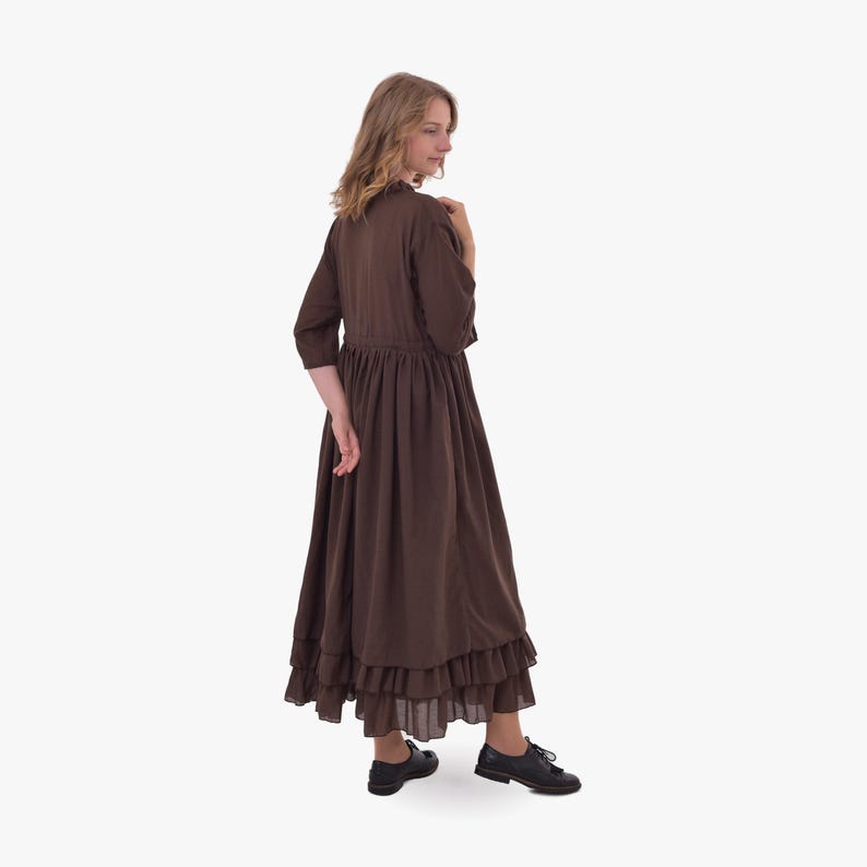 Pode incluir: Um vestido castanho com bainha com babados e mangas tr&ecirc;s-quartos. O vestido tem cintura franzida e &eacute; combinado com sapatos pretos. O estilo evoca uma est&eacute;tica vintage ou campestre.