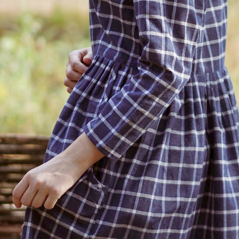Puede incluir: Un vestido de cuadros azules y blancos con cintura fruncida y un bolsillo de parche. El vestido tiene mangas largas y un ajuste holgado.