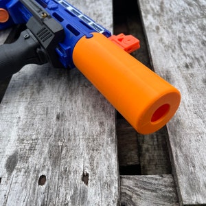 May include: A blue and orange toy gun with a black handguard and an orange barrel extension. The gun is lying on a wooden surface.