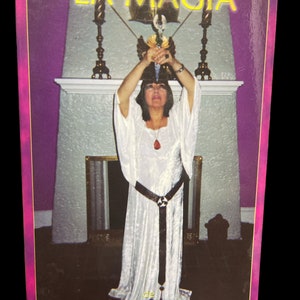 May include: A book cover with a woman in a white robe holding a sword in front of a fireplace. The title of the book is "LA MAGIA" and the author is "MIGENE GONZALEZ-WIPPLER".