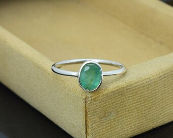 May include: A silver ring featuring a vibrant green oval-cut gemstone. The ring has a thin, polished band and a bezel setting that securely holds the emerald. The gemstone's color is a rich, deep green.