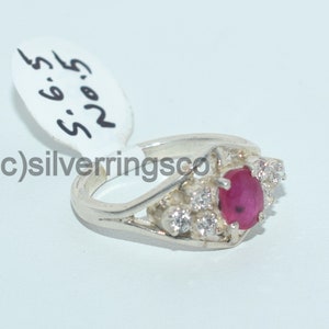 Pu&ograve; includere: Un anello d'argento con una pietra rossa circondata da pietre bianche pi&ugrave; piccole. L'anello &egrave; su uno sfondo bianco con un'etichetta che dice "R.O.S. 5.6.5".