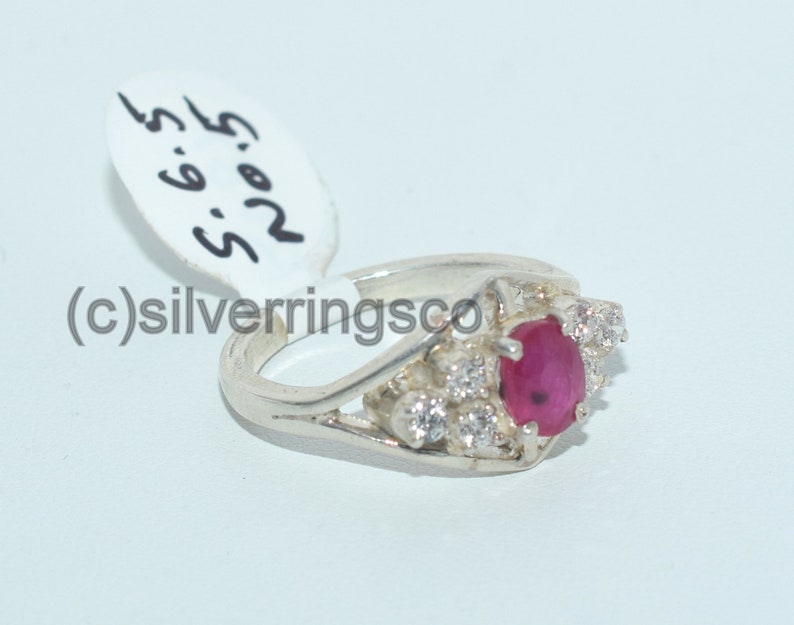 Pu&ograve; includere: Un anello d'argento con una pietra rossa circondata da pietre bianche pi&ugrave; piccole. L'anello &egrave; su uno sfondo bianco con un'etichetta che dice "R.O.S. 5.6.5".