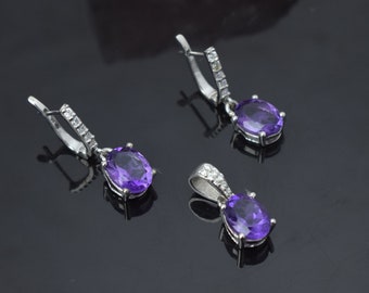 Könnte beinhalten: Ein silbernes Halsketten- und Ohrring-Set mit violetten ovalen Edelsteinen und klaren Zirkonia-Akzenten.