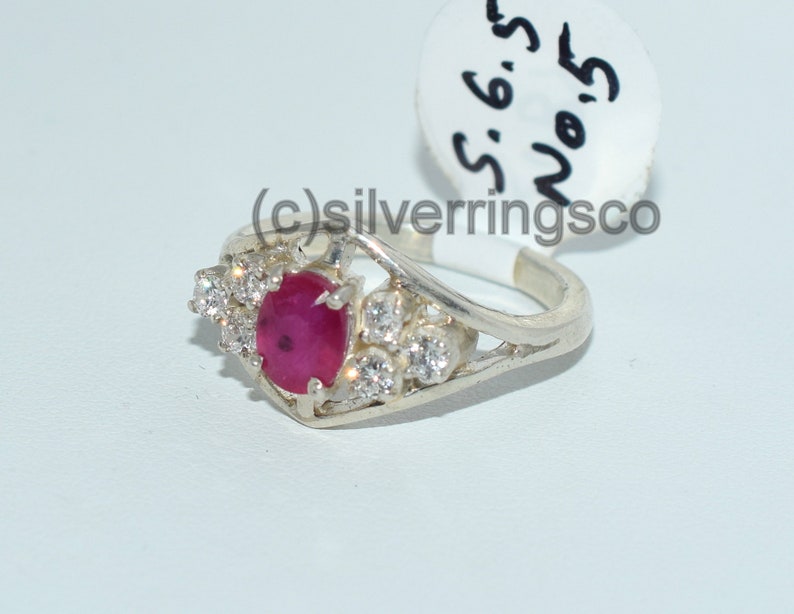 Pu&ograve; includere: Un anello d'argento con una pietra preziosa di rubino rosso e pietre di zircone cubico chiare. L'anello &egrave; taglia 6,5.