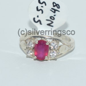 May include: A silver ring featuring a red oval gemstone and smaller white gemstones. The ring is engraved with the text "S.S. No.48".