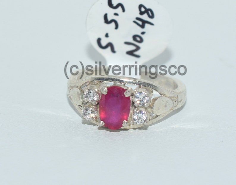 May include: A silver ring featuring a red oval gemstone and smaller white gemstones. The ring is engraved with the text "S.S. No.48".