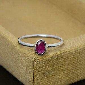Puede incluir: Un anillo de plata con una vibrante gema de rubí ovalada. El anillo presenta una banda delgada y un engaste de bisel que sujeta firmemente la gema roja. El diseño es simple y elegante, adecuado para el uso diario u ocasiones especiales.