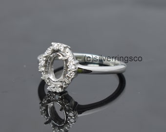 Puede incluir: Un anillo de plata con un engaste redondo de forma ovalada rodeado de pequeños diamantes. El anillo está diseñado para contener una piedra preciosa.