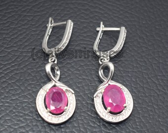 May include: A pair of silver dangle earrings with a pink oval gemstone surrounded by smaller clear gemstones. The earrings have a simple, elegant design.