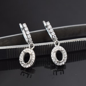 May include: A pair of silver hoop earrings with a dangling oval pendant. Each earring is adorned with small, clear cubic zirconia stones.