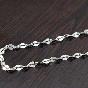 May include: A silver chain necklace with oval-shaped links. The chain is on a dark brown surface.
