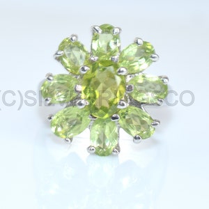 May include: A silver ring with a floral design, set with oval-cut peridot gemstones. The ring's setting and band are silver. The peridot stones are a bright, light green, arranged in a flower shape with a central, larger stone. The ring is a piece of jewellery.