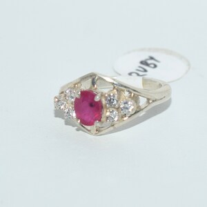 Pu&ograve; includere: Un anello d'argento con una pietra preziosa rossa e pietre bianche pi&ugrave; piccole. L'anello ha un design delicato e intricato.