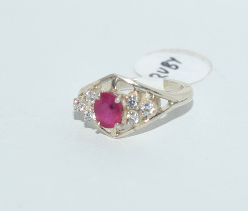 Pu&ograve; includere: Un anello d'argento con una pietra preziosa rossa e pietre bianche pi&ugrave; piccole. L'anello ha un design delicato e intricato.