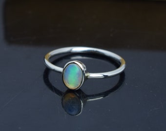 Pode incluir: Um anel de prata com uma pedra de opala oval. A opala exibe uma mistura de cores, incluindo verde, azul e amarelo. O anel tem uma banda fina e um design simples e elegante, adequado para uso diário.