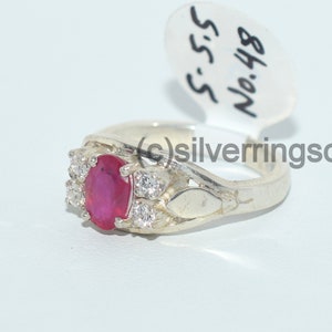 May include: A silver ring featuring a red oval gemstone surrounded by smaller white gemstones. The ring is marked with the number "848" and the letters "S.S.S."