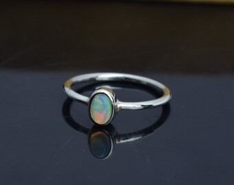 Pode incluir: Um anel de prata com uma pedra preciosa de opala oval. A opala exibe uma mistura de cores, incluindo branco, amarelo e azul. O anel tem uma banda fina e um design simples e elegante, adequado para uso diário.