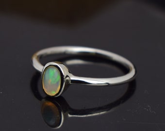 Pode incluir: Um anel de prata com uma pedra de opala oval. A opala exibe cores verdes, amarelas e brancas. O anel tem um design simples e elegante, perfeito para uso diário.