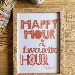 May include: A framed print with the text "Happy Hour is my favourite Hour Cheers!" in a peachy orange color. The print is in a light wood frame.