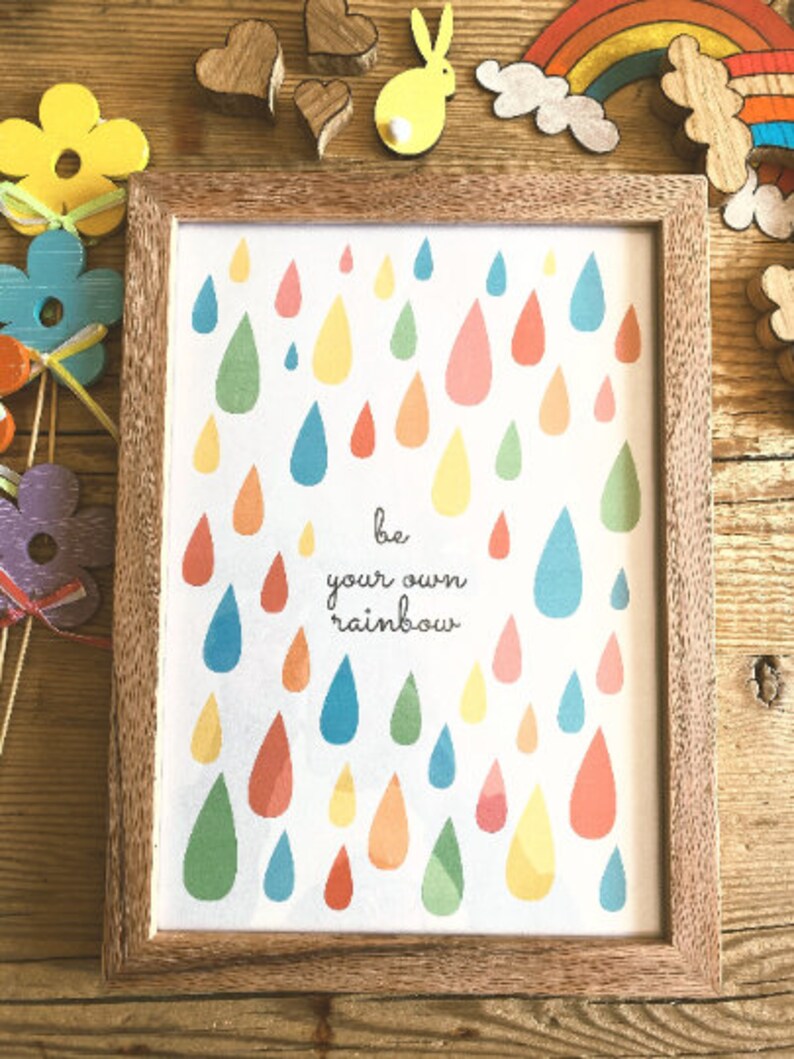 May include: A framed print with a white background and colorful raindrops. The print says "be your own rainbow".