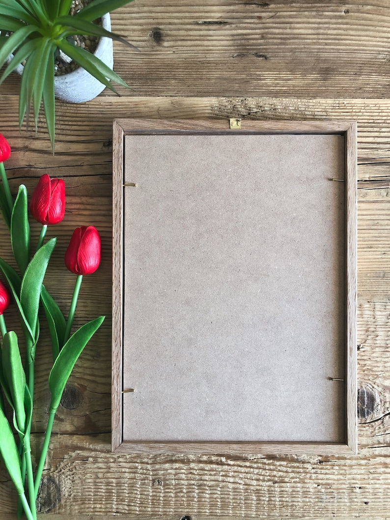 May include: A brown wooden picture frame with a light brown cardboard backing. The frame is sitting on a wooden surface.