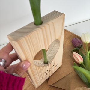 Puede incluir: Jarrón de madera con una abertura en forma de corazón y el texto "Soy la mia idea de la felicidad" grabado en el lateral. El jarrón está hecho de madera natural y tiene un aspecto rústico.