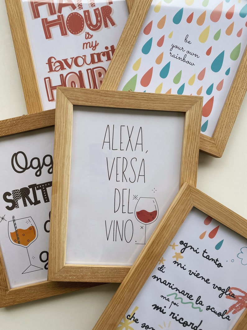 May include: Four framed prints with different designs. The top left print says "Happy Hour is my favorite hour". The top right print has a rainbow of raindrops with the text "Be your own rainbow". The bottom left print has a glass of a spritzer with the text "Oggi Spritz". The bottom right print has a glass of red wine with the text "Alexa, versa del vino".