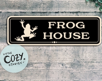 Może przedstawiać: Czarno-biały znak z sylwetką żaby i tekstem "FROG HOUSE".