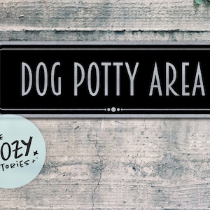 Peut inclure: Une plaque rectangulaire noire aux coins arrondis avec une fine bordure blanche. Le texte DOG POTTY AREA est imprimé dans une police blanche sans empattement. Une petite ligne décorative horizontale avec trois points est centrée.