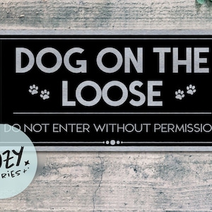 Può includere: Un cartello rettangolare nero con la scritta "DOG ON THE LOOSE" in grandi lettere argentate. Il cartello include anche impronte di zampe e la scritta "DO NOT ENTER WITHOUT PERMISSION". Un piccolo logo rotondo si trova nell'angolo in basso a sinistra.